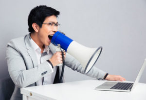 Businessman sitting at table and screaming in megaphone on laptop while content marketing